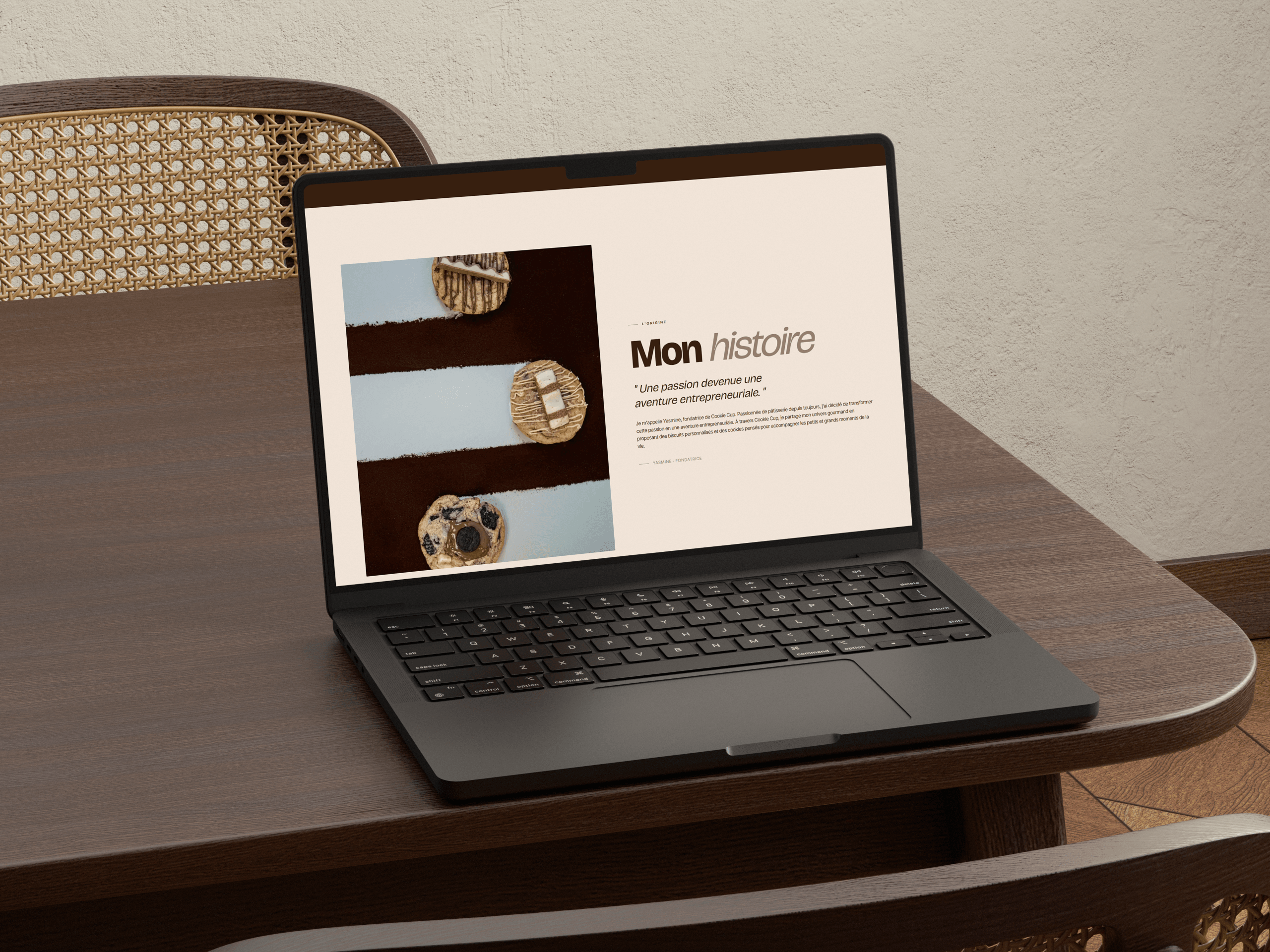 Page « Mon histoire » du site Cookie Cup sur un portable posé sur une table en bois, à côté d’une chaise cannée.