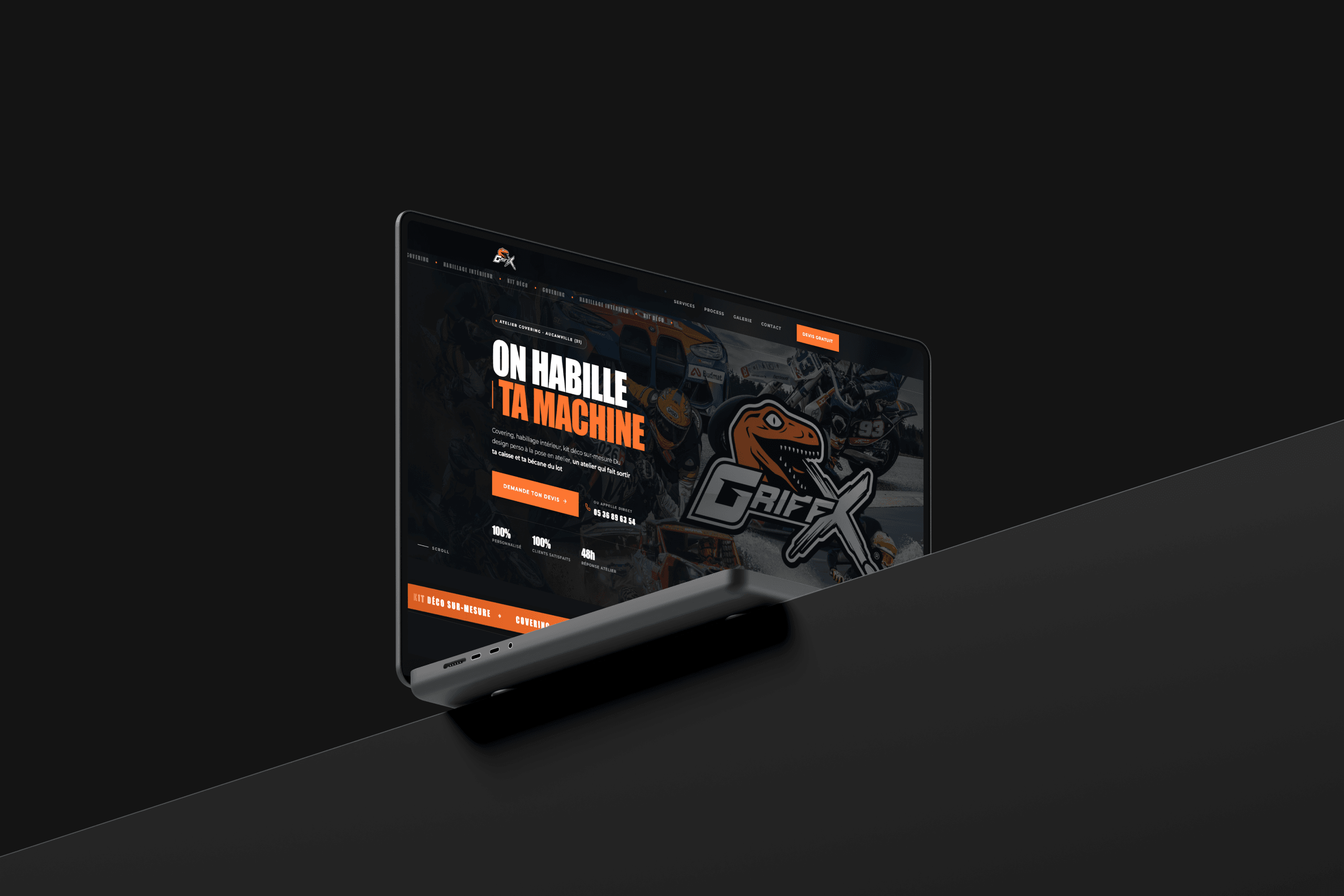 Page d'accueil du site GriffX sur écran incliné : l'accroche « On habille ta machine » en blanc et orange, et le logo au lettrage griffé sur fond sombre.