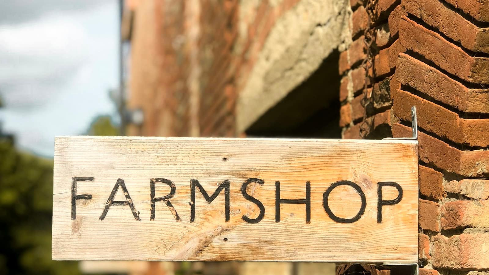 Enseigne en bois gravée « Farmshop », accrochée à un mur de briques